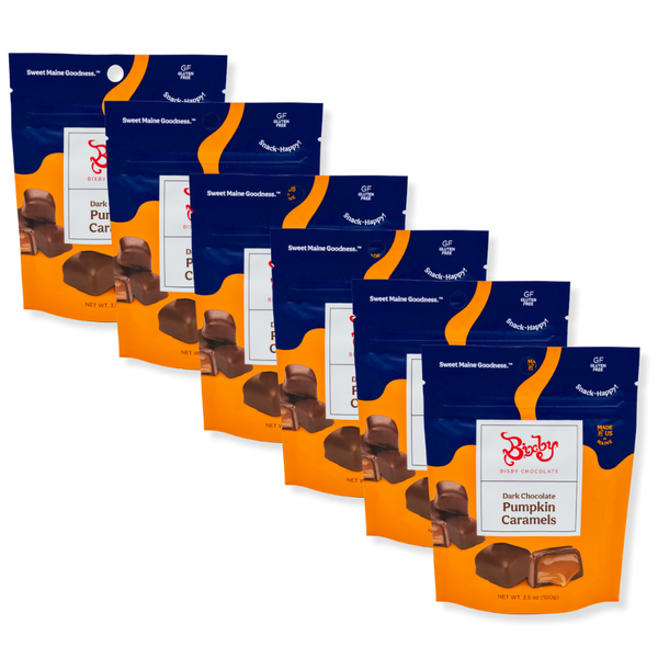 Six pouches of Bixby Chocolates Pumpkin Caramels are displayed in a diagonal row, with orange and blue packaging showing chocolate-covered caramels and labeled "Gluten Free" and "Sweet Maine Goodness.