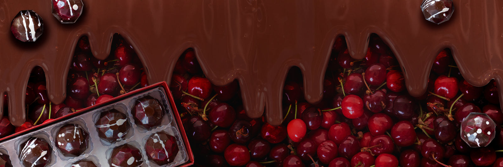 A layer of melted chocolate drips over a pile of fresh red cherries, with a box of chocolate-covered cherries in the bottom left corner and several chocolate pieces scattered on top.