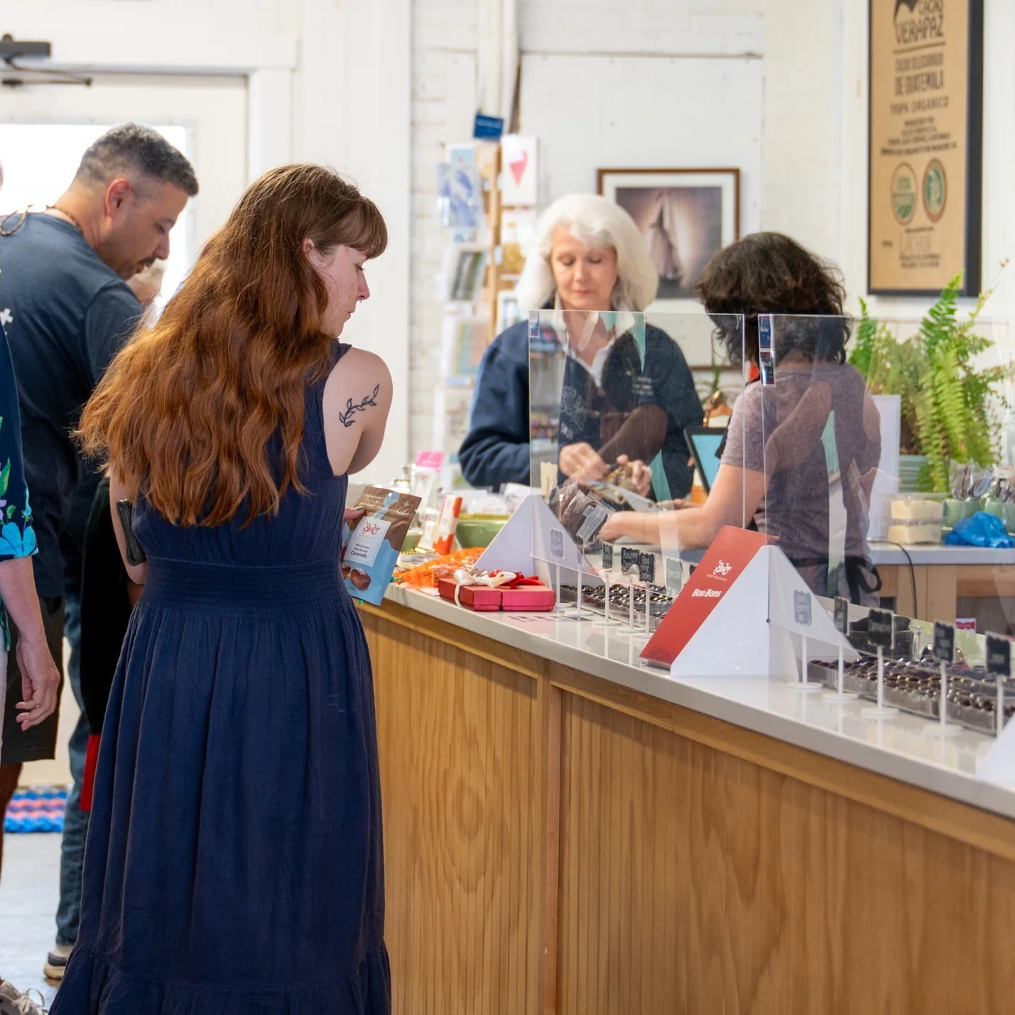 People shopping at a store with a focus on a woman in a blue dress.