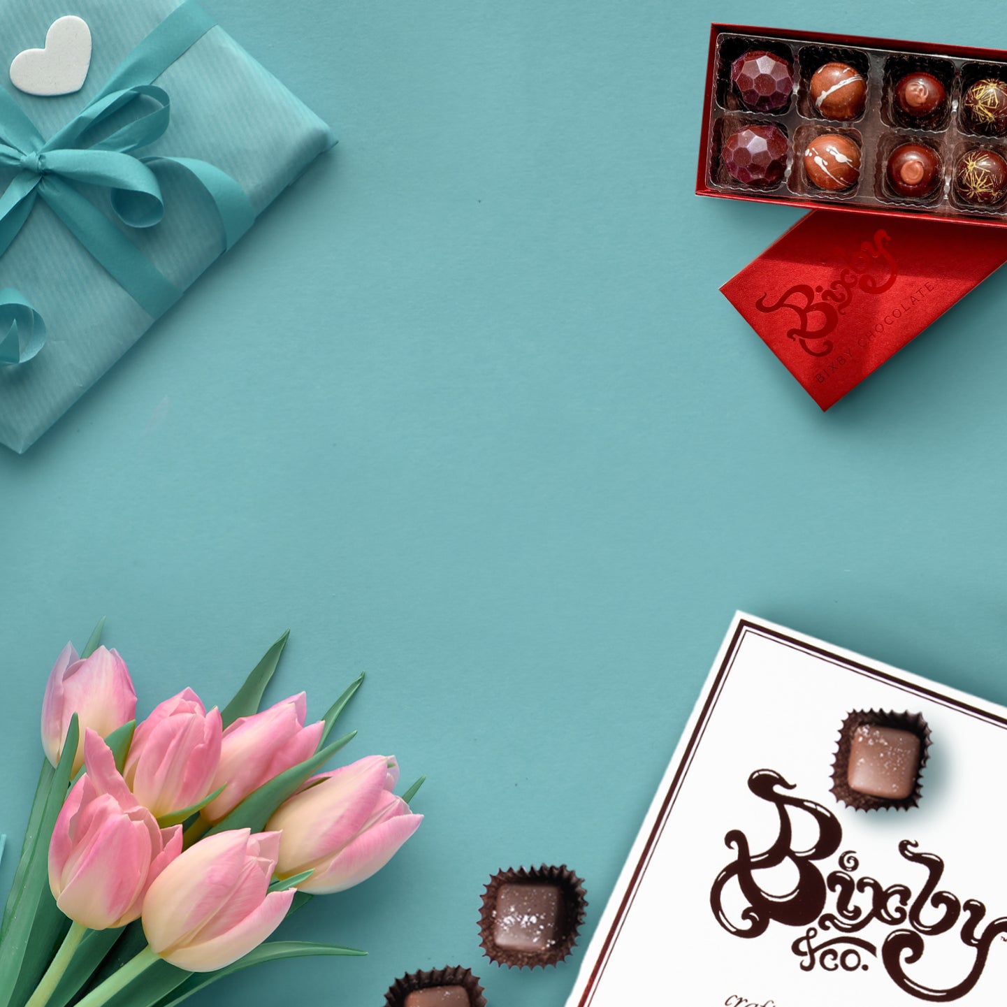 An arrangement of pink tulips, a wrapped gift with a heart, an open red box of assorted chocolates, and a white chocolate box on a light blue background.