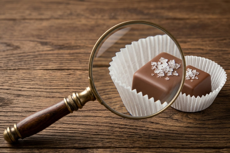 Magnifying glass on a wooden table focusing on a piece of chocolate.