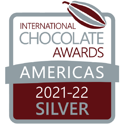 Logo for the International Chocolate Awards Americas, showing a cocoa bean and text reading 2021-22 Silver. The award recognizes chocolate excellence across the Americas region.