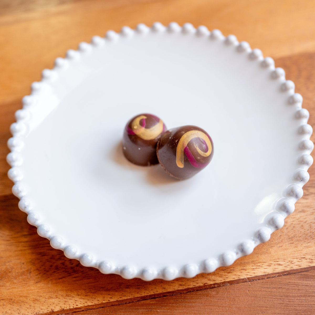 Two peanut butter and jelly bon bons with swirl patterns on a white plate on a wooden surface