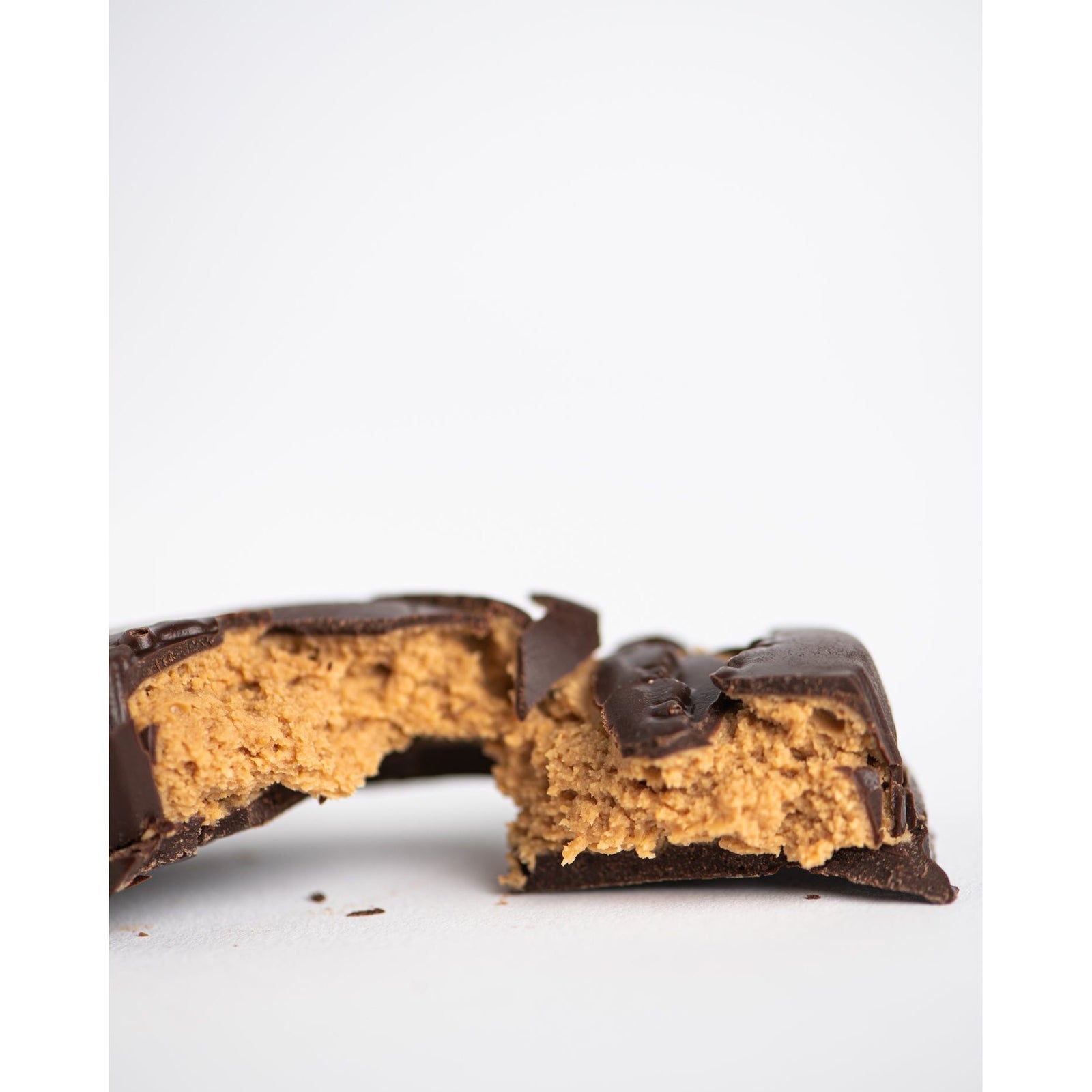 A close-up of a chocolate candy bar broken in half, revealing a creamy, light brown peanut butter filling inside. The background is plain white.